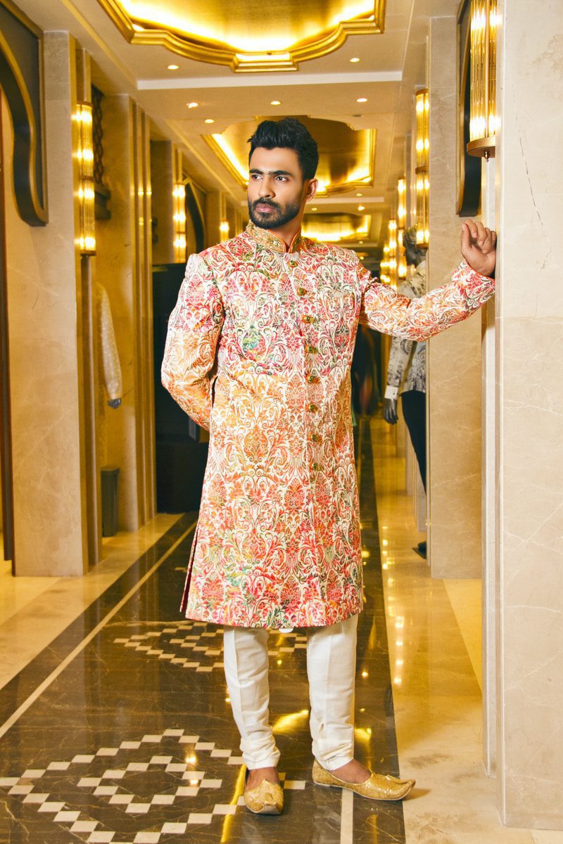 man in pink and white floral wedding shwerwani standing on hallway