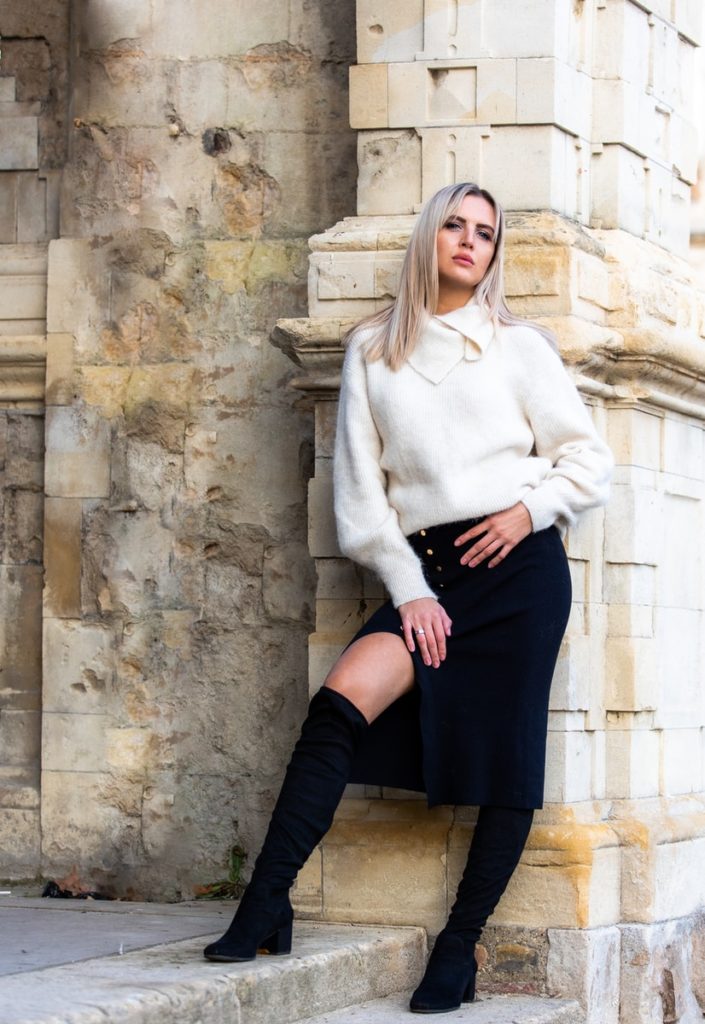 woman in white sweater and black skirt sitting on concrete wall during daytime